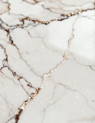 The primary subject of the image is a marble countertop with a gold-like pattern on it. The setting is a kitchen or bathroom, as the countertop is a part of a counter. The visual style is a close-up of the marble countertop, showcasing its unique design. The colors and mood of the image are elegant and sophisticated, with the gold-like pattern adding a touch of luxury to the marble surface.