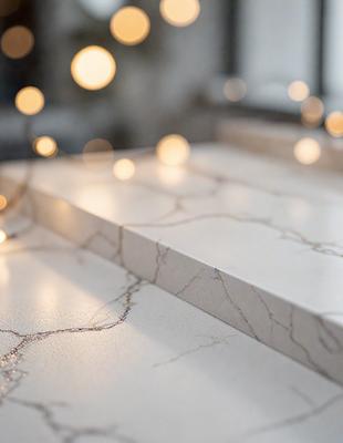 The primary subject of the image is a marble countertop with a white surface. The setting is a room with a white wall behind the countertop. The visual style is a photo, and the colors and mood are predominantly white, giving the scene a clean and elegant appearance.