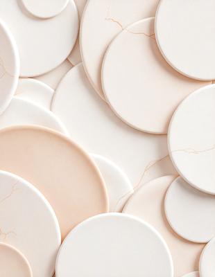 The primary subject of the image is a collection of white ceramic plates. The plates are arranged in a visually appealing manner, creating a sense of harmony and balance. The setting is a white background, which provides a clean and minimalist look to the scene. The visual style is a close-up of the plates, showcasing their intricate details and textures. The colors and mood of the image are predominantly white, giving it a clean, fresh, and elegant appearance.