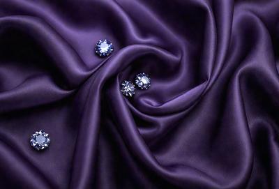 The primary subject of the image is a purple fabric with a pattern of small diamond-shaped crystals. The setting is a close-up view of the fabric, showcasing its texture and pattern. The visual style is a detailed, up-close representation of the fabric. The colors and mood of the image are predominantly purple, with the diamond-shaped crystals adding a touch of sparkle and sophistication.