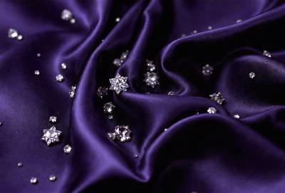 The primary subject of the image is a purple fabric with a pattern of diamond shapes. The setting is a close-up view of the fabric, showcasing the intricate design. The visual style is a realistic representation of the fabric, with no indication of digital art or illustration. The colors and mood of the image are predominantly purple, giving it a sophisticated and elegant appearance.