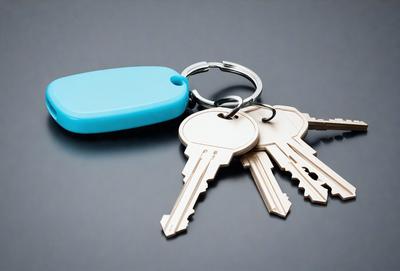The primary subject of the image is a pair of keys. The keys are placed on a gray surface, which serves as the setting or background. The visual style of the image is a photo, capturing the details of the keys and the surface they are placed on. The colors in the image are predominantly gray, giving the scene a neutral and simple atmosphere.