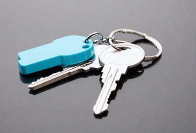 The primary subject of the image is a pair of keys, which are silver and blue in color. The keys are placed on a gray surface, which serves as the setting or background of the image. The visual style of the image is a close-up of the keys, showcasing their details and colors. The overall atmosphere of the image is simple and straightforward, focusing on the keys as the main object of interest.