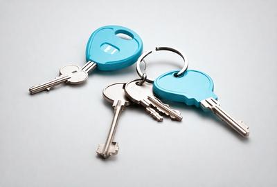 The primary subject of the image is a pair of blue keys. The keys are placed on a white surface, which serves as the setting or background. The visual style of the image is a photo, capturing the details of the keys. The dominant colors in the image are blue and white, creating a clean and simple atmosphere.