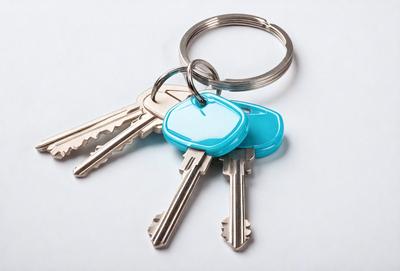 The primary subject of the image is a set of keys, which are the main objects in the scene. The keys are placed on a white surface, which serves as the background. The visual style of the image is a photo, capturing the details of the keys and the background. The colors in the image are predominantly silver and blue, giving the scene a clean and modern appearance.