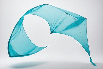 The primary subject of the image is a large, blue, curved kite. The kite is suspended in the air, and it appears to be made of a mesh-like material. The setting is a white background, which provides a clean and uncluttered environment for the kite to be displayed. The visual style of the image is a combination of photo and digital art, as it captures the kite's unique shape and structure. The colors and mood of the image are predominantly blue, which adds