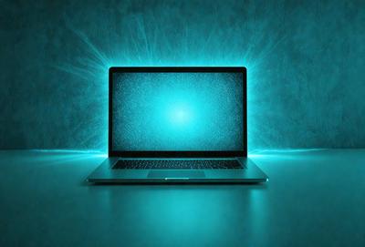 The primary subject of the image is a laptop computer. The laptop is placed on a table, and it is turned on, displaying a blue screen. The setting is a room with a blue wall, which adds to the overall atmosphere of the image. The visual style is a photo, capturing the laptop in its natural environment. The colors and mood of the image are predominantly blue, creating a calm and focused atmosphere.
