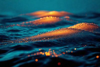 The primary subject of the image is a body of water, possibly an ocean, with a blue hue. The setting is a dark blue background, which contrasts with the light blue water. The visual style is a combination of a photo and digital art, creating a unique and captivating scene. The colors and mood of the image are predominantly blue, with a hint of orange, giving it a serene and calming atmosphere.