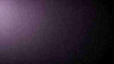 The primary subject of the image is a purple wall. The setting is a dark room, and the visual style is a close-up of the purple wall. The colors and mood of the image are predominantly purple, creating a calm and serene atmosphere.