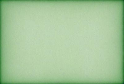 The primary subject of the image is a large, green sheet of paper. The setting is a white background, which creates a clean and minimalist appearance. The visual style is a close-up of the paper, emphasizing its texture and color. The colors and mood of the image are predominantly green, giving it a calm and serene atmosphere.