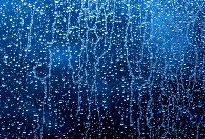 The primary subject of the image is a rainy day, as evidenced by the raindrops on the window. The setting is an indoor environment, with the raindrops falling on a window. The visual style is a photo, capturing the raindrops on the window. The colors and mood of the image are predominantly blue, with the raindrops creating a soothing and calming atmosphere.