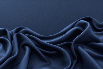 The primary subject of the image is a blue fabric, which is the main object, scene, or focus of the image. The setting or background is a dark blue surface, which provides a contrasting backdrop for the fabric. The visual style of the image is a close-up of the blue fabric, showcasing its texture and details. The colors and mood of the image are predominantly blue, creating a calm and serene atmosphere.
