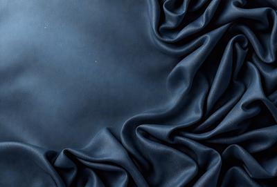 The primary subject of the image is a blue fabric, which is the main object, scene, or focus of the image. The setting or background is a dark blue cloth, and the visual style is a photo. The colors and mood of the image are predominantly dark blue, creating a moody and dramatic atmosphere.