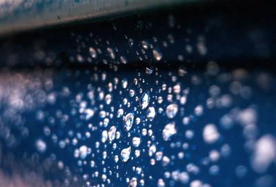 The primary subject of the image is a close-up of a blue surface with water droplets on it. The setting appears to be a dark room, and the visual style is a photo. The dominant colors are blue and white, creating a calm and serene atmosphere.