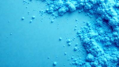 The primary subject of the image is a blue substance, possibly a powder or a liquid, that is spread across a surface. The setting appears to be a white background, which contrasts with the blue substance. The visual style of the image is a close-up of the blue substance, showcasing its texture and details. The dominant colors in the image are blue and white, creating a calm and soothing atmosphere.
