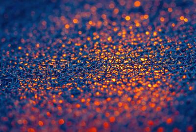 The primary subject of the image is a close-up of a blue surface with a pattern of bright orange lights. The setting appears to be a dark room, and the visual style is a combination of a photo and digital art. The dominant colors are blue and orange, creating a vibrant and lively atmosphere.