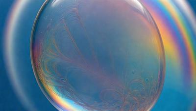 The primary subject of the image is a large, colorful, and swirling bubble. The bubble is floating in a blue background, which adds to the overall atmosphere of the scene. The visual style of the image is a combination of photo and digital art, creating a unique and captivating visual experience. The colors and mood of the image are vibrant and lively, with the swirling patterns of the bubble adding a sense of movement and energy to the scene.