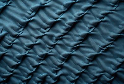 The primary subject of the image is a blue fabric with a pattern of waves. The setting is a close-up of the fabric, showcasing its texture and design. The visual style is a detailed, textured image of the blue fabric. The colors and mood of the image are predominantly blue, creating a calm and soothing atmosphere.