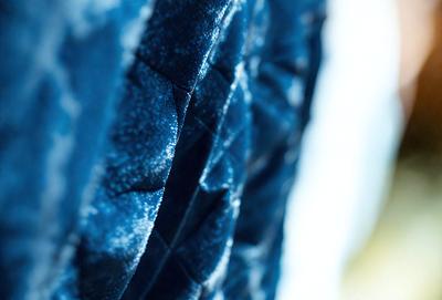 The primary subject of the image is a blue fabric with a pattern of white and blue dots. The setting is a close-up of the fabric, showcasing its intricate design. The visual style is a combination of a photo and digital art, as the image appears to be a close-up of a patterned fabric. The colors and mood of the image are predominantly blue, with the white dots adding a touch of brightness and contrast.