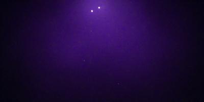 The image features a purple sky with a few stars visible. The primary subject is the night sky, which is the main focus of the image. The setting is a dark, starry night, and the visual style is a natural, outdoor scene. The colors and mood of the image are predominantly purple, creating a serene and peaceful atmosphere.