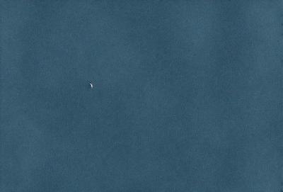 The primary subject of the image is a small moon, which is visible in the sky. The setting is a vast, dark blue sky, with no clouds or other objects obstructing the view of the moon. The visual style of the image is a photo, capturing the moon in its natural environment. The colors and mood of the image are predominantly dark and moody, with the blue sky providing a contrasting backdrop to the moon.