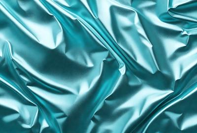 The primary subject of the image is a close-up of a blue fabric, possibly a piece of silk or a similar material. The setting is a dark background, which contrasts with the blue fabric. The visual style appears to be a photo, as the fabric is captured in detail. The colors and mood of the image are predominantly blue, creating a calm and serene atmosphere.