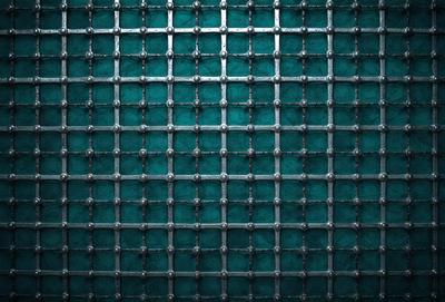 The primary subject of the image is a blue and silver metal grid. The setting is a dark blue background, which contrasts with the silver metal grid. The visual style is a close-up of the grid, showcasing its intricate design. The colors and mood of the image are dark and moody, with the blue background and silver metal grid creating a sense of depth and complexity.