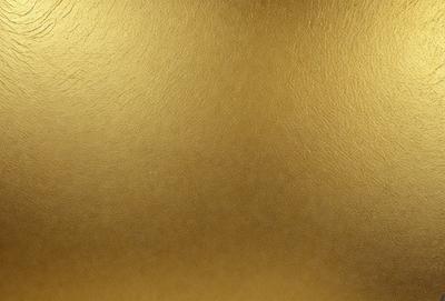 The primary subject of the image is a close-up of a shiny, golden surface. The setting is a wall, and the visual style is a photo. The dominant colors are gold and brown, creating a warm and luxurious atmosphere.