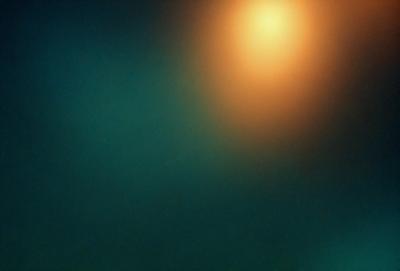 The primary subject of the image is a bright orange light, which is the main focus of the scene. The setting is a dark, foggy environment, with a greenish-blue background. The visual style appears to be a photo, capturing the unique light source in the darkness. The colors and mood of the image are dominated by the contrasting orange light and the surrounding dark, foggy atmosphere.
