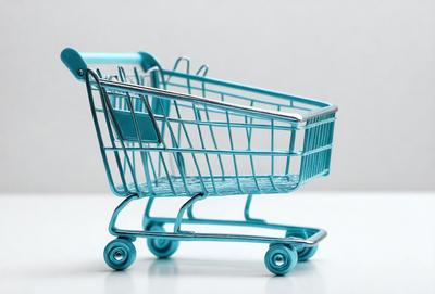 The primary subject of the image is a blue shopping cart. The cart is placed on a white surface, which serves as the background. The visual style of the image is a photo, capturing the cart in its natural environment. The dominant colors in the image are blue and white, creating a clean and modern atmosphere.