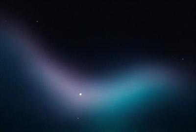 The primary subject of the image is a purple, blue, and green light streak in the sky. The setting is a dark night with a few stars visible in the background. The visual style appears to be a digital art or illustration, as the light streak is depicted in a unique and artistic manner. The colors and mood of the image are predominantly dark and mysterious, with the purple, blue, and green light streak adding a touch of whimsy and wonder to the scene.