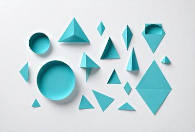 The primary subject of the image is a collection of blue geometric shapes, including triangles and diamonds, arranged on a white surface. The setting appears to be a white wall, and the visual style is a combination of digital art and illustration. The dominant colors in the image are blue and white, creating a clean and modern atmosphere.
