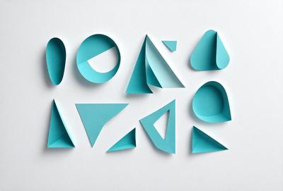 The primary subject of the image is a collection of blue geometric shapes, which are displayed on a white surface. The shapes are arranged in various orientations, creating a visually interesting and artistic composition. The setting appears to be a studio or workspace, where the artist has created these unique designs. The visual style of the image is a combination of digital art and illustration, showcasing the artist's creativity and skill in crafting these geometric patterns. The dominant colors in the image are blue and white, which contribute to a