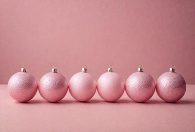 The primary subject of the image is a row of six pink ornaments, which appear to be Christmas ornaments. They are arranged in a straight line on a pink surface, which could be a table or a wall. The visual style of the image is a close-up of the ornaments, showcasing their details and colors. The colors and mood of the image are predominantly pink, creating a warm and festive atmosphere.