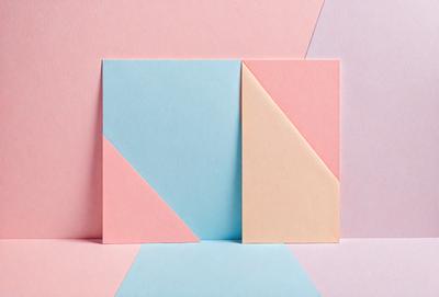 The primary subject of the image is a pink, blue, and yellow paper. The paper is folded into a triangle shape, and it is placed on a pink background. The visual style of the image is a close-up of the paper, showcasing its colors and texture. The overall atmosphere of the image is bright and cheerful, with the vibrant colors of the paper creating a lively and inviting scene.