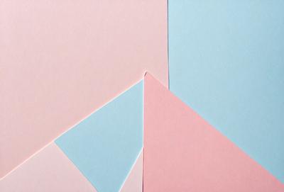 The primary subject of the image is a blue, pink, and white paper. The paper is cut into a triangular shape, and it is placed on a pink background. The visual style of the image is a close-up of the paper, showcasing its unique design. The colors and mood of the image are predominantly pink and blue, creating a warm and inviting atmosphere.