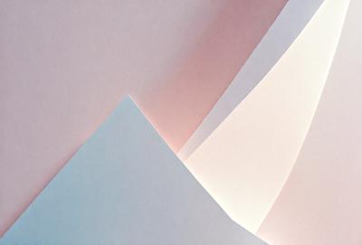 The primary subject of the image is a stack of white paper. The setting is a pink background, which adds a contrasting color to the scene. The visual style is a close-up of the paper, showcasing its texture and details. The colors and mood of the image are predominantly white and pink, creating a clean and elegant atmosphere.