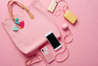 The primary subject of the image is a pink purse with a cell phone and a calculator inside. The setting is a pink background, and the visual style is a photo. The colors and mood of the image are predominantly pink, creating a warm and feminine atmosphere.