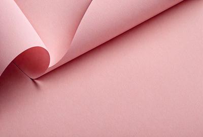 The primary subject of the image is a pink sheet of paper with a red dot on it. The setting is a pink background, which creates a contrast with the red dot. The visual style is a close-up of the paper, showcasing the red dot and the pink paper. The colors and mood of the image are predominantly pink, creating a warm and inviting atmosphere.