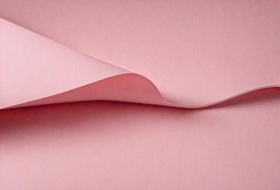 The primary subject of the image is a piece of pink paper. The setting is a pink background, which creates a warm and inviting atmosphere. The visual style is a close-up of the paper, showcasing its texture and color. The colors and mood of the image are predominantly pink, giving it a soft and delicate appearance.