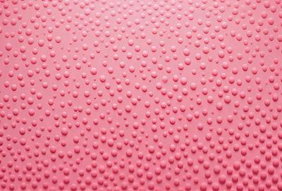 The primary subject of the image is a close-up of a pink surface with a pattern of small, round bumps or dots. The setting appears to be a pink wall or a similar background. The visual style of the image is a close-up, which emphasizes the details of the bumps on the surface. The colors and mood of the image are predominantly pink, creating a warm and inviting atmosphere.