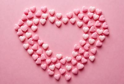 The primary subject of the image is a heart-shaped arrangement of pink and white hearts. The hearts are scattered across a pink background, creating a visually appealing and romantic display. The visual style of the image is a combination of photo and digital art, as it appears to be a close-up of the heart arrangement. The colors and mood of the image are predominantly pink and white, giving it a warm and loving atmosphere.