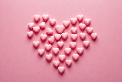 The primary subject of the image is a heart-shaped arrangement of pink hearts. The hearts are placed on a pink background, creating a visually appealing and romantic scene. The visual style of the image is a combination of photo and digital art, as it appears to be a close-up of the heart arrangement. The dominant colors in the image are pink, which creates a warm and loving atmosphere.