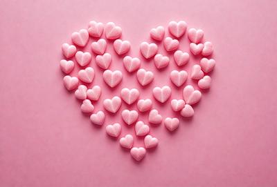 The primary subject of the image is a heart-shaped arrangement of pink hearts. The hearts are placed on a pink background, creating a visually appealing and romantic scene. The visual style of the image is a combination of photo and digital art, as it appears to be a close-up of the heart arrangement. The dominant colors in the image are pink, which gives the scene a warm and loving atmosphere.