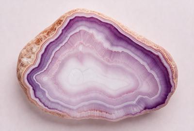 The primary subject of the image is a large, purple, multi-colored rock. The rock is placed on a white surface, which serves as the setting or background. The visual style of the image is a close-up of the rock, showcasing its unique and colorful patterns. The dominant colors in the image are purple and white, creating a striking and eye-catching appearance.