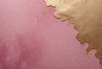 The primary subject of the image is a pink wall with gold paint splatters on it. The setting is a room with a pink background. The visual style is a close-up of the wall, showcasing the gold paint splatters. The colors and mood of the image are predominantly pink and gold, creating a warm and inviting atmosphere.