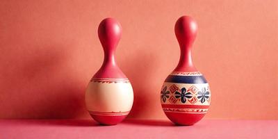 The primary subject of the image is a pair of colorful vases, which are placed on a pink surface. The vases are decorated with blue and red patterns, and they are positioned next to each other. The setting appears to be a room with a wall, and the visual style is a combination of photo and digital art. The colors and mood of the image are vibrant and lively, with the pink surface and the bold colors of the vases creating a cheerful atmosphere.