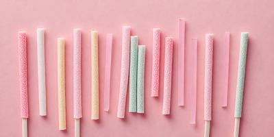 The primary subject of the image is a row of colorful, patterned lollipops. The lollipops are arranged in a neat line, with each one featuring a different color and pattern. The setting is a pink background, which adds a vibrant and cheerful atmosphere to the scene. The visual style of the image is a close-up of the lollipops, showcasing their details and colors. Overall, the image conveys a fun and playful mood.