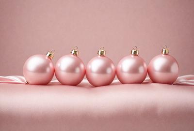 The primary subject of the image is a row of six pink ornaments, which are likely Christmas ornaments. They are arranged in a line on a pink surface, which could be a table or a couch. The setting appears to be indoors, and the visual style is a close-up of the ornaments. The colors and mood of the image are predominantly pink, creating a warm and festive atmosphere.