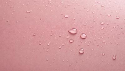 The primary subject of the image is a pink surface with water droplets on it. The setting is a pink background, and the visual style is a close-up of the pink surface with water droplets. The colors and mood of the image are predominantly pink, creating a warm and inviting atmosphere.